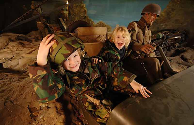 Children in an Army Jeep with a life-sized model soldier at the wheel..